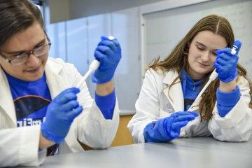 Students Nathan Rice ’24 and Lexi Lumley ’24 conduct research in labcoats and blue gloves.