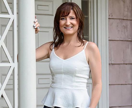 Nationally-recognized speaker, author, and entrepreneur, Jaime Spencer, stands on front porch and smiles.